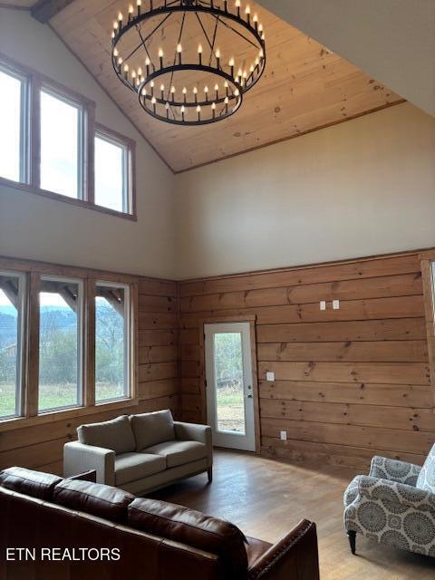 living room with wood walls, wooden ceiling, lofted ceiling, an inviting chandelier, and wood-type flooring