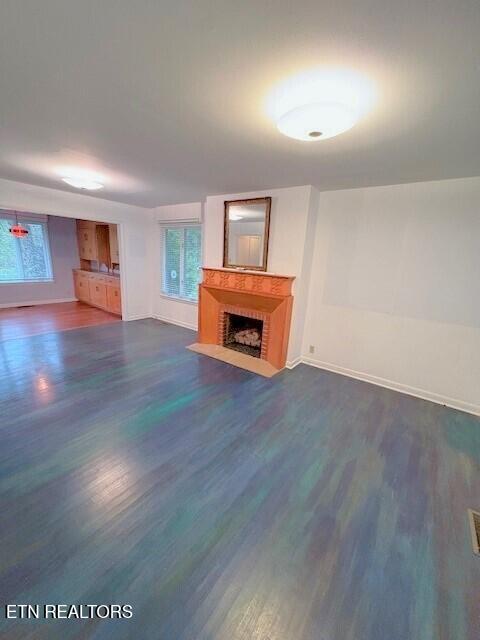 unfurnished living room with dark wood-type flooring, plenty of natural light, and a fireplace