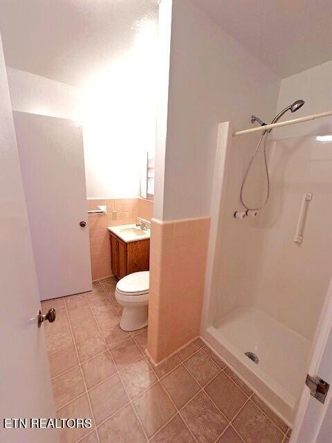 bathroom with tile walls, vanity, a shower, and toilet