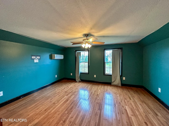 empty room featuring an AC wall unit, a textured ceiling, ceiling fan, and light hardwood / wood-style floors