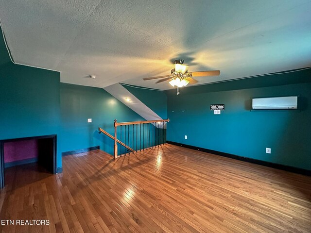 bonus room with wood-type flooring, a textured ceiling, a wall unit AC, and ceiling fan