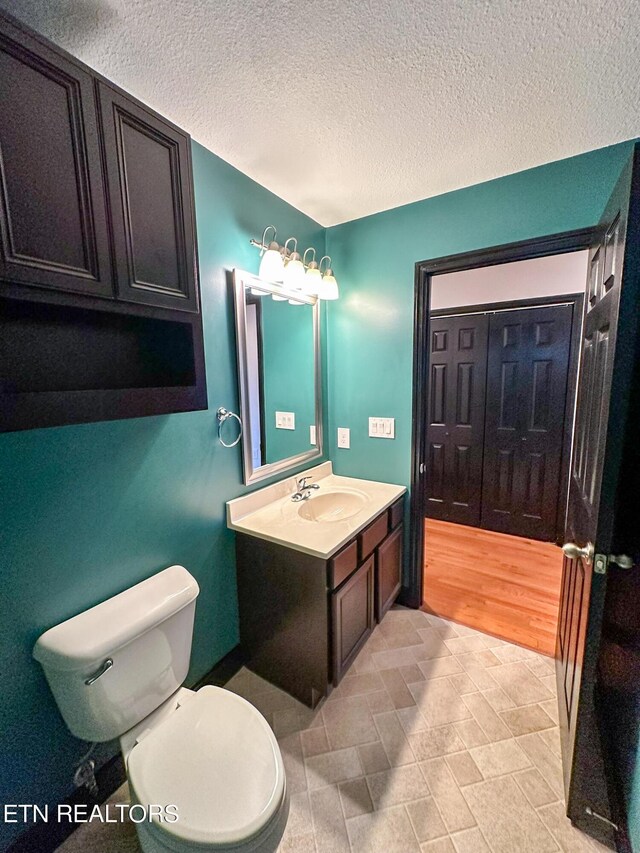 bathroom featuring wood-type flooring, toilet, vanity, and a textured ceiling