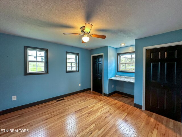 unfurnished bedroom with multiple windows, light wood-type flooring, and a textured ceiling