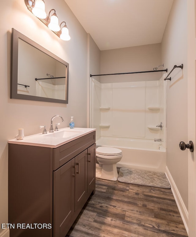 bathroom featuring baseboards, toilet, wood finished floors, vanity, and shower / washtub combination