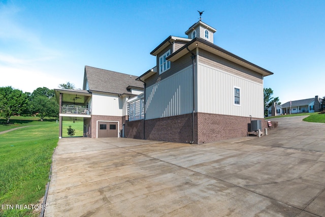 view of side of home featuring central air condition unit, a garage, brick siding, driveway, and a lawn