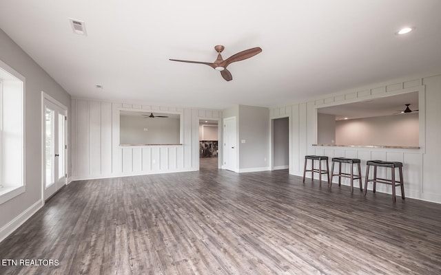 unfurnished living room with a ceiling fan, dark wood-style flooring, visible vents, and baseboards