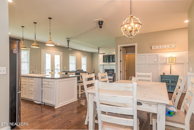 dining space featuring a chandelier, a decorative wall, dark wood-style flooring, a fireplace, and french doors