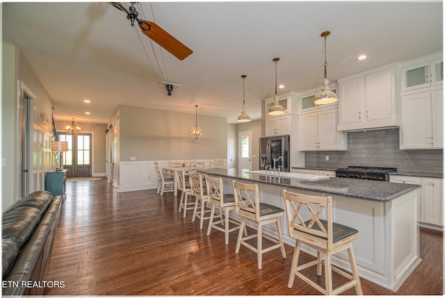 kitchen featuring a center island with sink, a kitchen bar, glass insert cabinets, open floor plan, and stainless steel fridge with ice dispenser