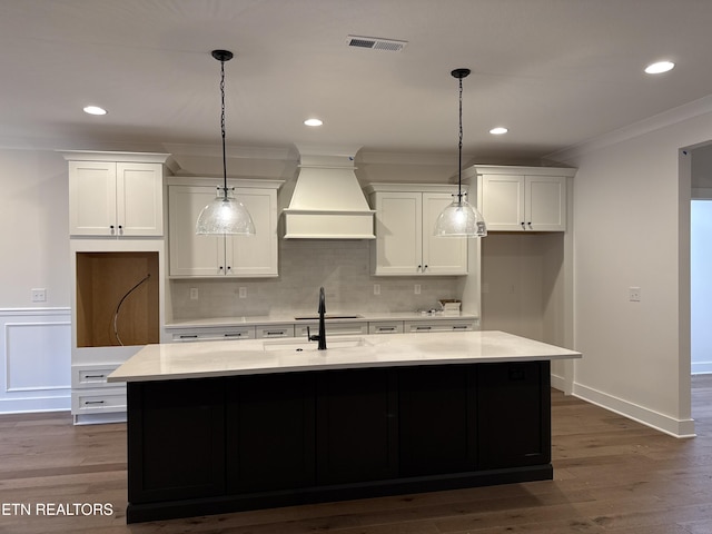 kitchen featuring ornamental molding, white cabinets, custom range hood, and an island with sink