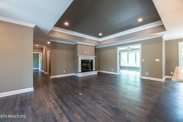 unfurnished living room with ceiling fan, dark hardwood / wood-style floors, ornamental molding, and a tray ceiling