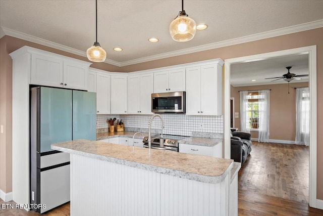 kitchen with tasteful backsplash, hardwood / wood-style floors, ornamental molding, a center island with sink, and appliances with stainless steel finishes