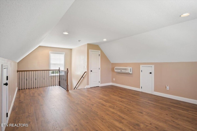 bonus room with a textured ceiling, an AC wall unit, lofted ceiling, and hardwood / wood-style floors