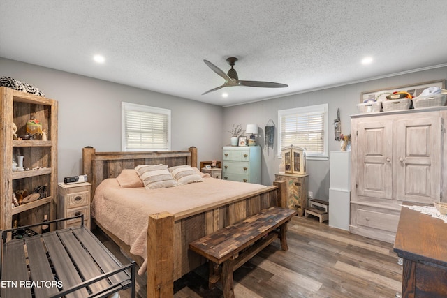 bedroom with a textured ceiling, multiple windows, wood-type flooring, and ceiling fan