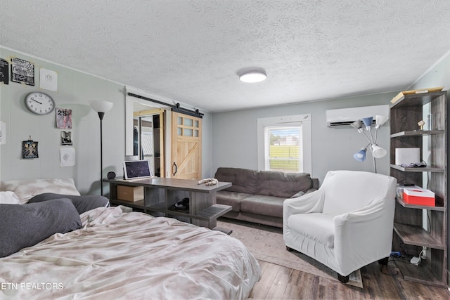 bedroom with hardwood / wood-style floors, a wall mounted AC, a textured ceiling, and a barn door