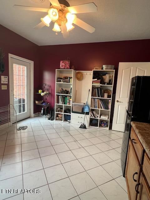 interior space featuring light tile patterned floors, ceiling fan, and black refrigerator