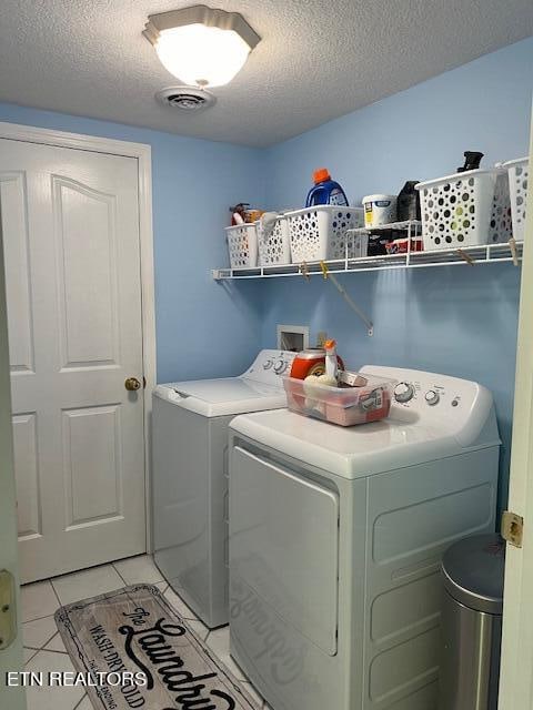 laundry area with light tile patterned floors, washing machine and clothes dryer, and a textured ceiling