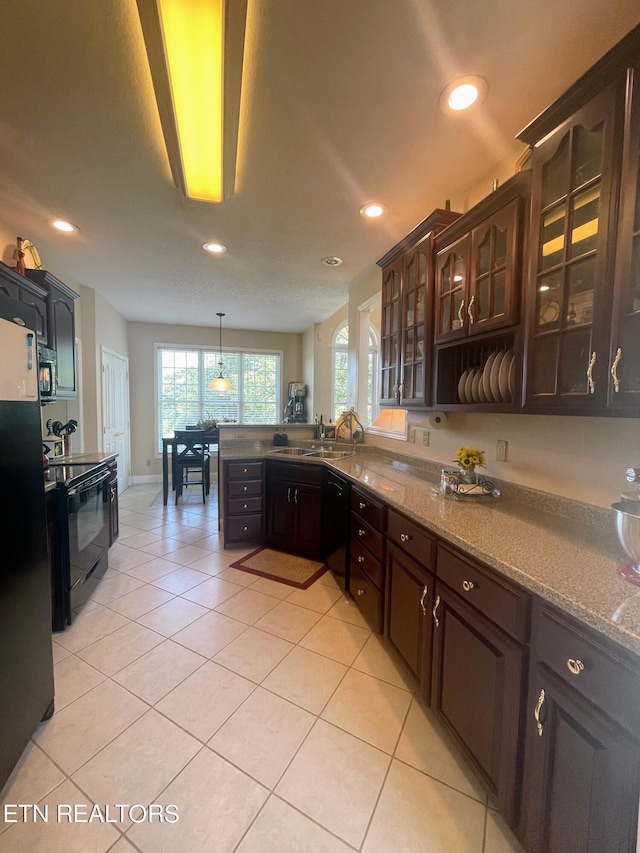 kitchen featuring dark brown cabinets, pendant lighting, black appliances, sink, and light stone counters