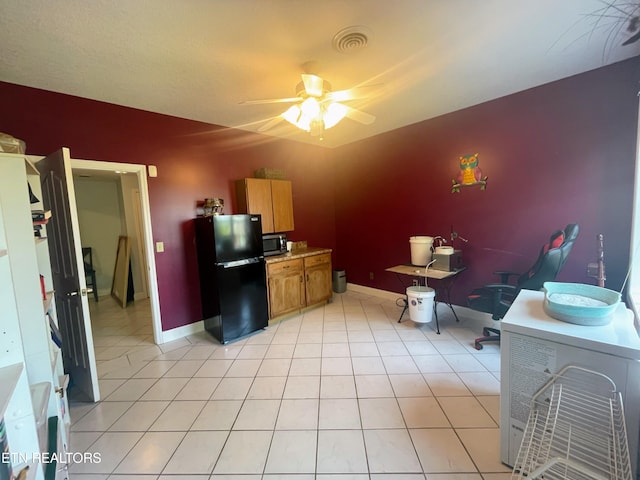 kitchen with light tile patterned floors, ceiling fan, and black fridge