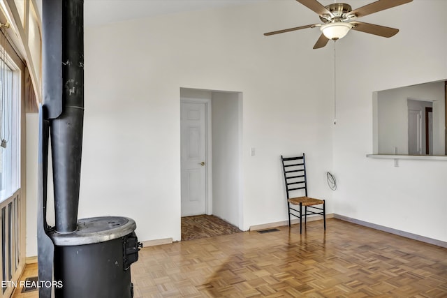 interior space featuring visible vents, baseboards, a wood stove, and a ceiling fan