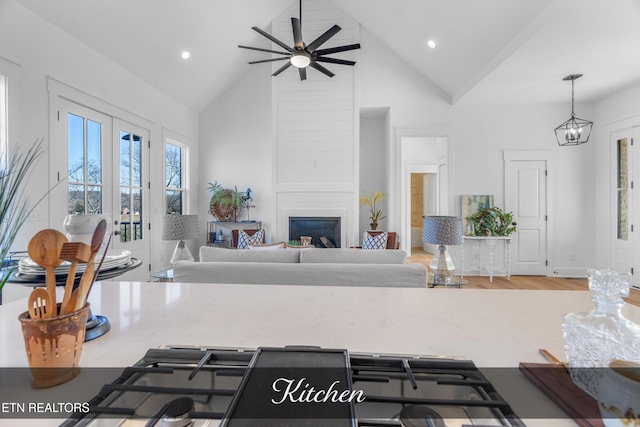 living room with ceiling fan with notable chandelier, high vaulted ceiling, a fireplace, and hardwood / wood-style flooring