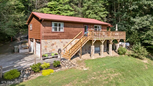 rear view of property featuring a yard, a garage, and a deck