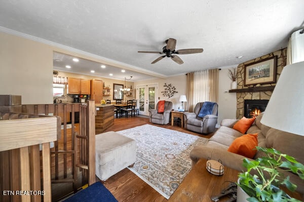 living room featuring a fireplace, wood-type flooring, ornamental molding, and ceiling fan