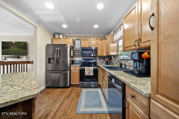 kitchen with decorative backsplash, light wood-type flooring, ornamental molding, sink, and appliances with stainless steel finishes