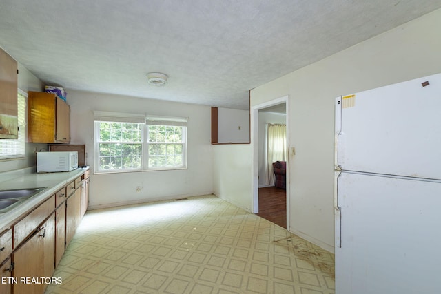 kitchen with a textured ceiling, light tile patterned floors, and white appliances