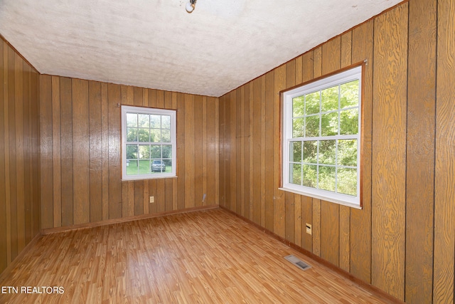 empty room featuring wood walls, light wood-type flooring, and a textured ceiling