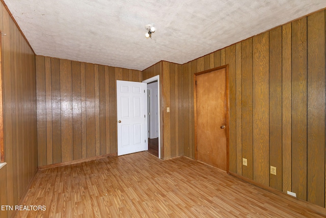 unfurnished room featuring a textured ceiling, wooden walls, and light hardwood / wood-style floors