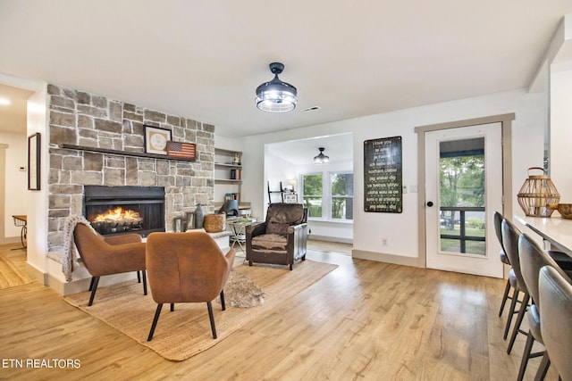 living room with visible vents, a stone fireplace, baseboards, and wood finished floors