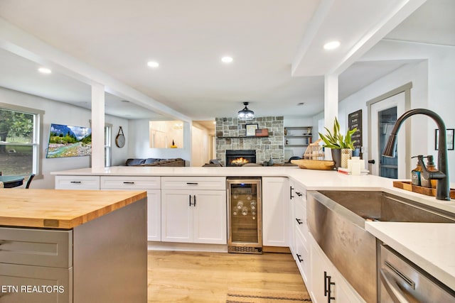 kitchen featuring butcher block counters, stainless steel dishwasher, open floor plan, white cabinetry, and beverage cooler