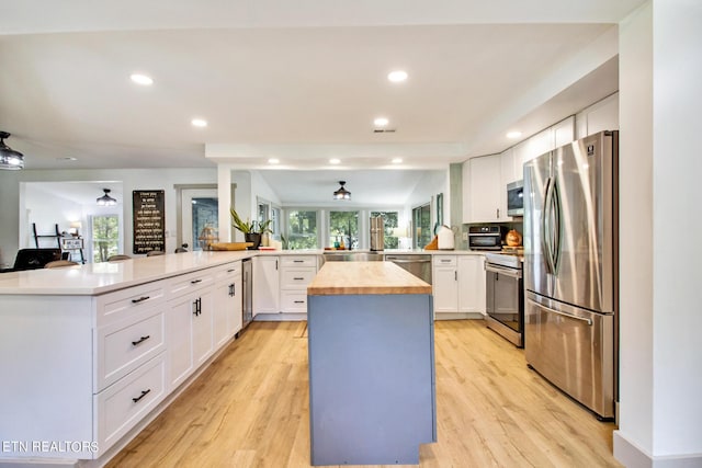 kitchen featuring appliances with stainless steel finishes, white cabinets, a peninsula, and light wood finished floors