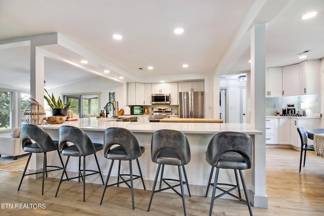 kitchen with a breakfast bar, light countertops, appliances with stainless steel finishes, white cabinetry, and a peninsula