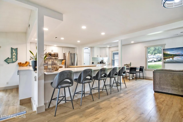 kitchen featuring white cabinets, a peninsula, stainless steel appliances, light countertops, and a kitchen bar