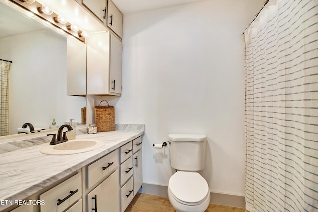 bathroom with curtained shower, toilet, wood finished floors, vanity, and baseboards