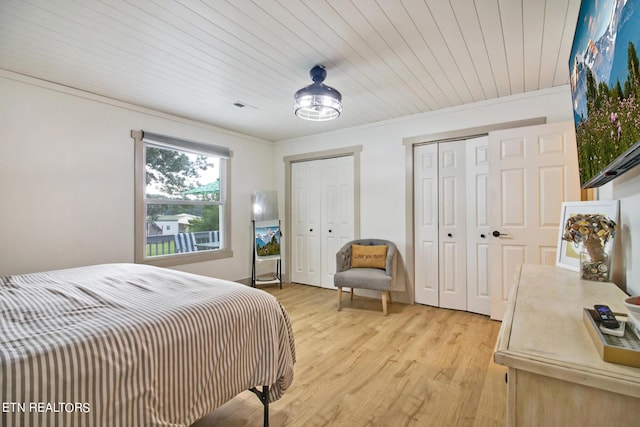 bedroom featuring two closets, visible vents, ornamental molding, light wood-type flooring, and wooden ceiling