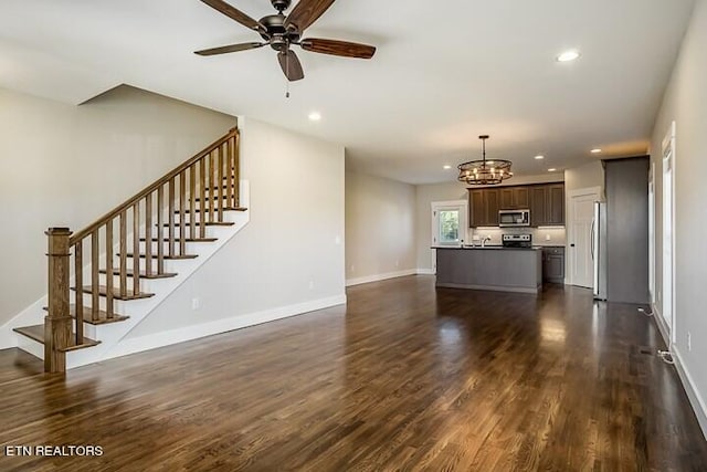 unfurnished living room with ceiling fan with notable chandelier and dark hardwood / wood-style floors