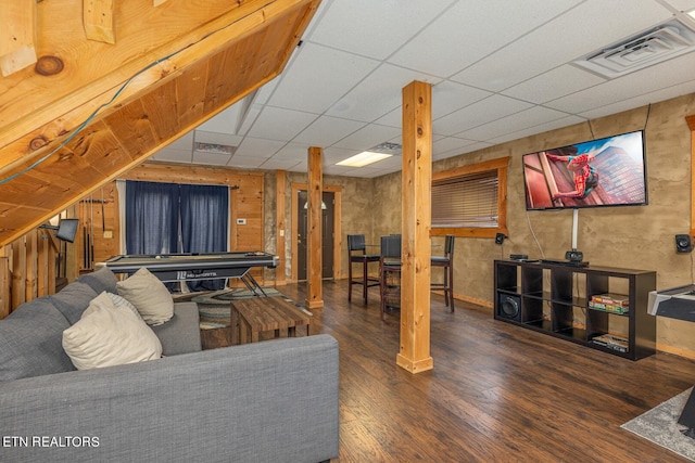 living room featuring a drop ceiling, hardwood / wood-style floors, and wooden walls