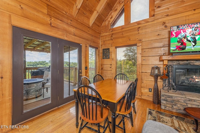 dining area with light wood-type flooring, a stone fireplace, vaulted ceiling with beams, and plenty of natural light