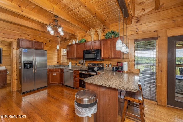 kitchen featuring appliances with stainless steel finishes, beamed ceiling, kitchen peninsula, light wood-type flooring, and wood walls