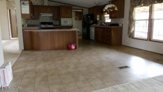 kitchen featuring black refrigerator, vaulted ceiling, kitchen peninsula, and tasteful backsplash