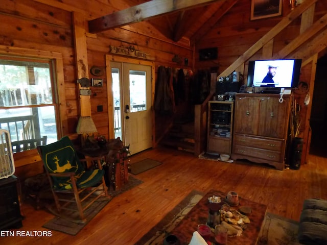 living room featuring vaulted ceiling with beams, wood-type flooring, wooden walls, and plenty of natural light