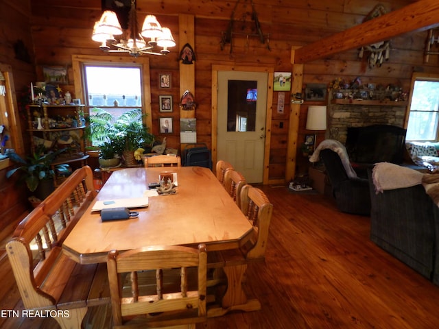 dining room featuring plenty of natural light, a stone fireplace, hardwood / wood-style floors, and a notable chandelier