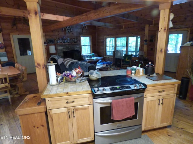 kitchen featuring a wealth of natural light, wooden walls, light brown cabinetry, stainless steel range with electric cooktop, and light hardwood / wood-style flooring