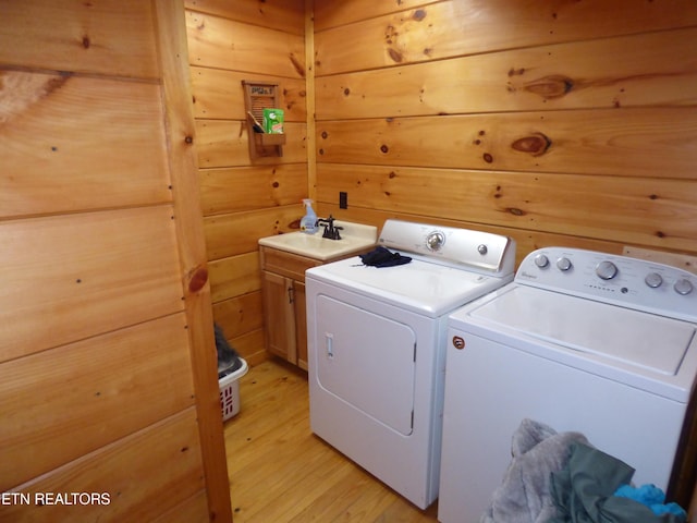 clothes washing area with washing machine and clothes dryer, sink, cabinets, light wood-type flooring, and wooden walls