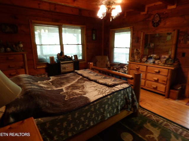 bedroom featuring wood-type flooring, wooden walls, a notable chandelier, and beam ceiling