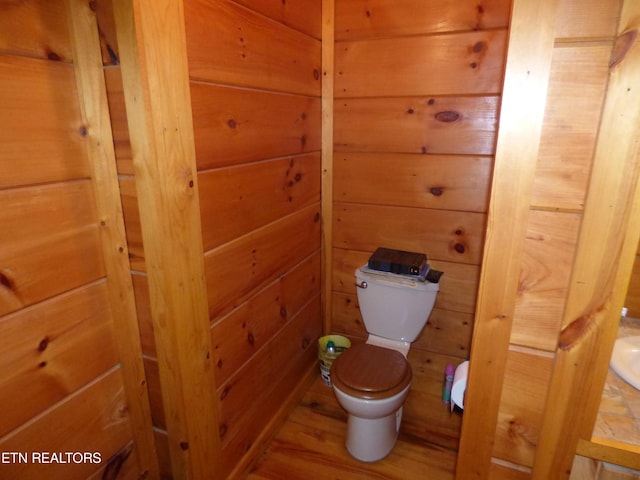 bathroom with hardwood / wood-style floors, wooden walls, and toilet