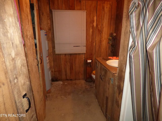 bathroom featuring toilet, vanity, wooden walls, and water heater