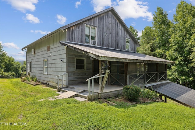 rear view of house with a sunroom, a lawn, and metal roof